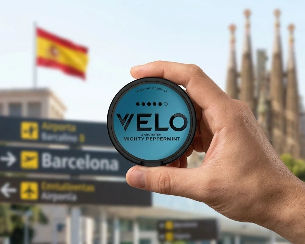 Mano che tiene una lattina di VELO Mighty Peppermint davanti ai cartelli stradali di Barcellona, una bandiera spagnola e la Sagrada Familia